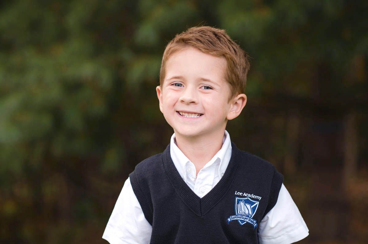 Group of school portraits showing young students wearing black uniforms with white collars against a natural background.