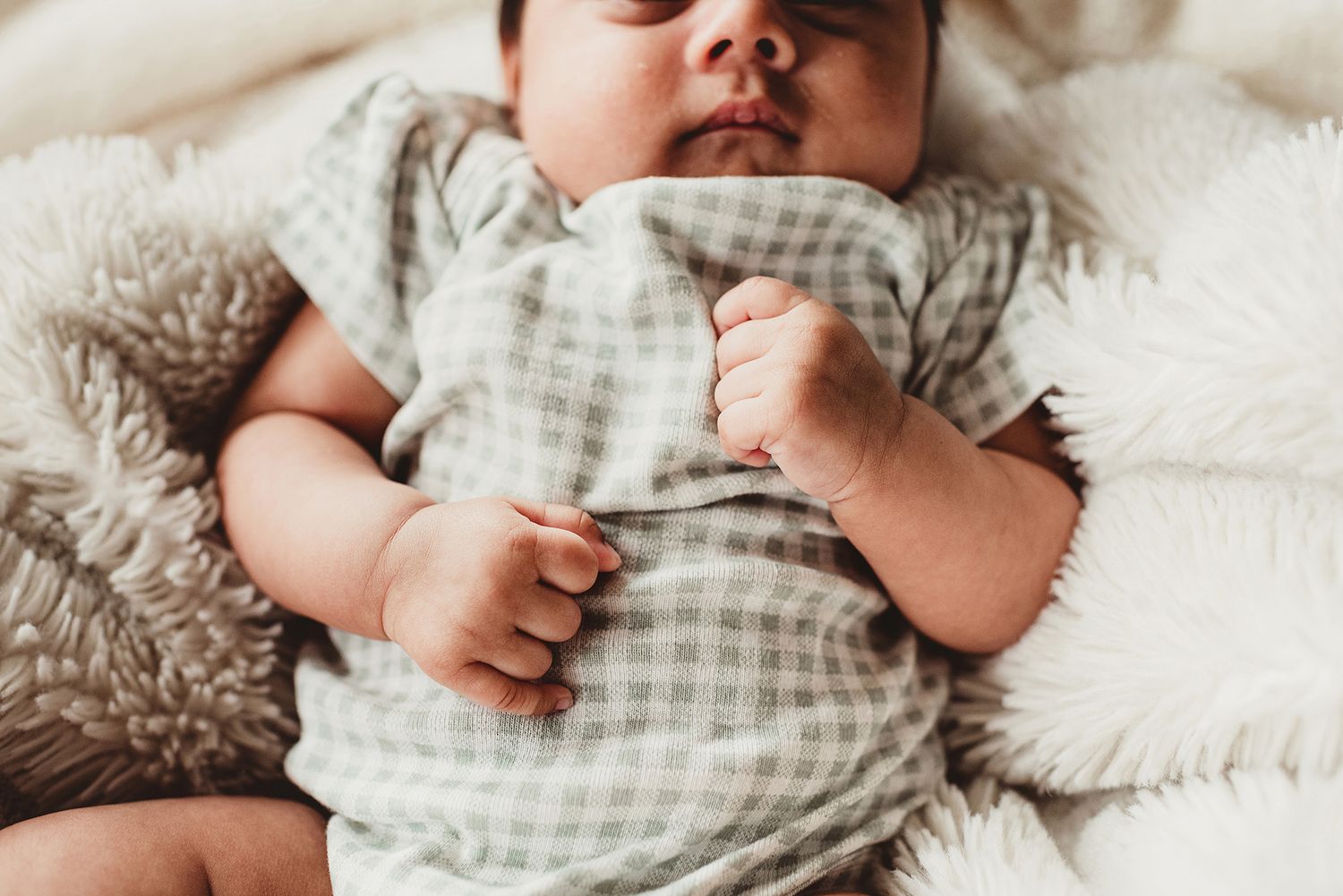 Baby in gingham outfit sleeping peacefully on soft white bedding.
