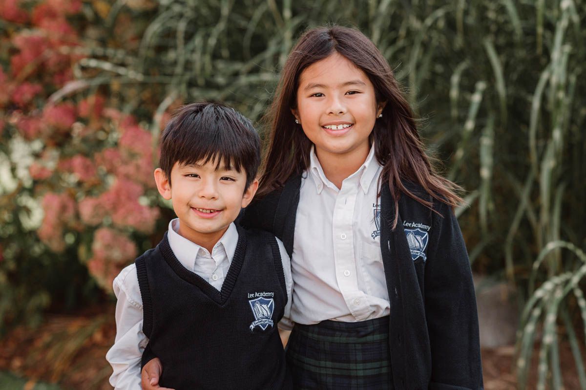 Students in school uniforms pose together outdoors with autumn foliage in the background.