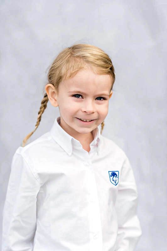 School portrait on grey background features bright white uniform with blue crest detail.