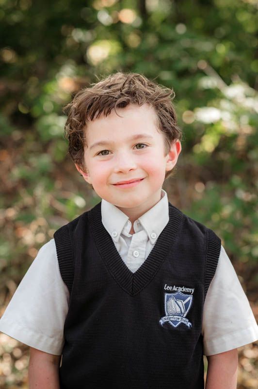 School portrait series showing student in navy sweater vest and white shirt with natural outdoor backdrop.