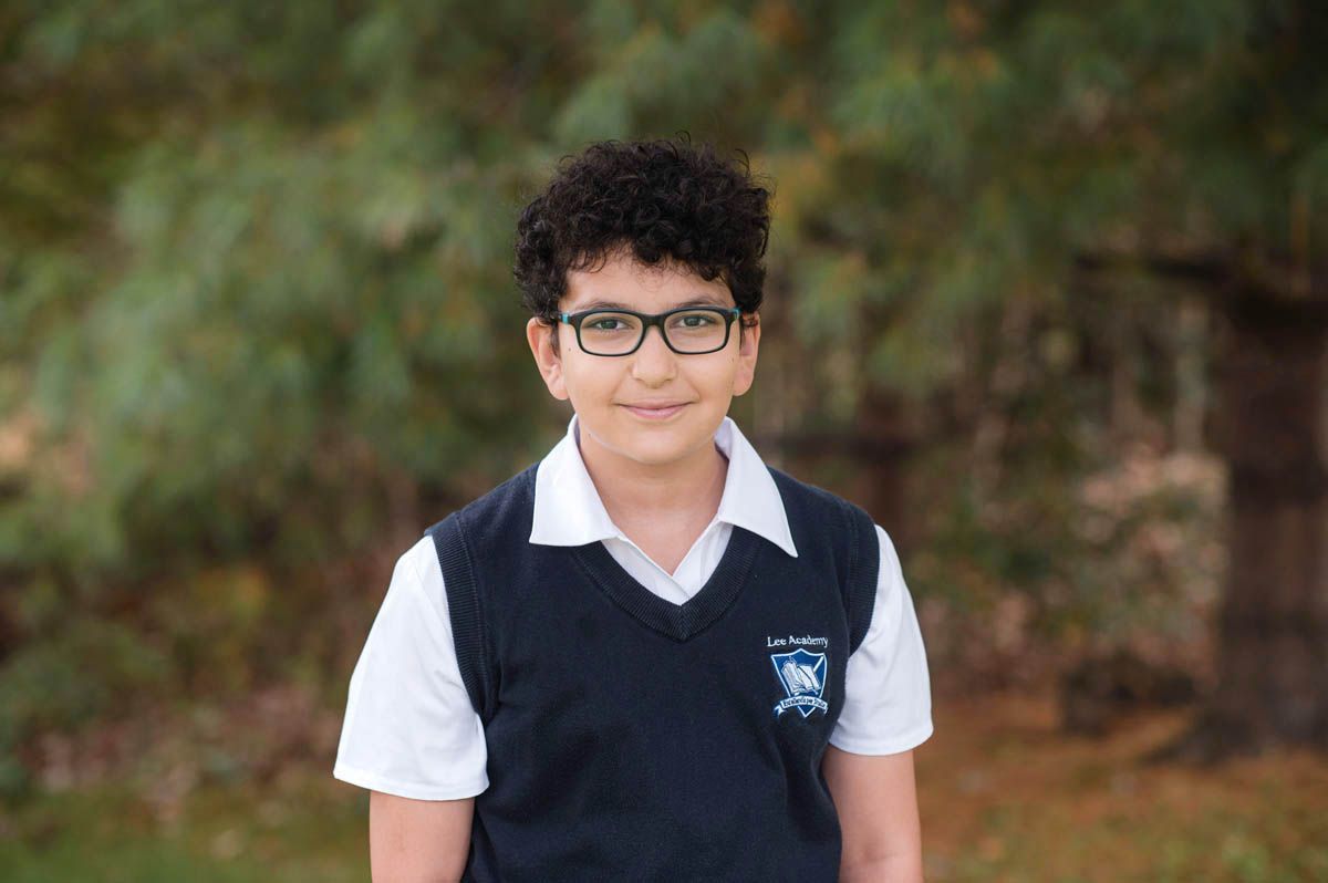 Student in school uniform with glasses poses for portrait photo outdoors.