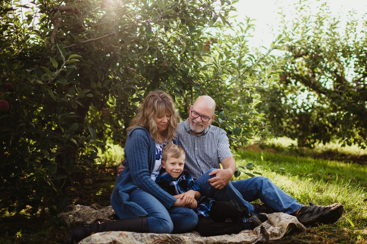 Family sitting together on a blanket in a sunlit apple orchard during autumn.