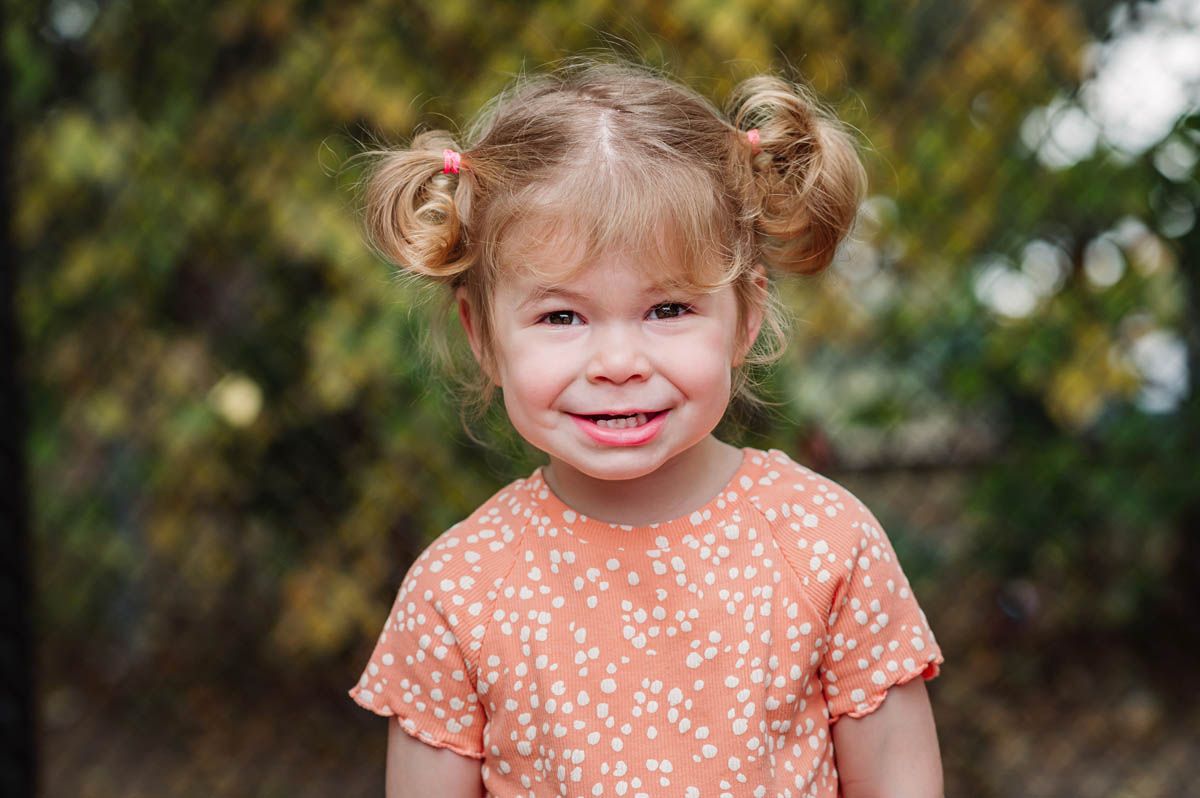 Young child wearing a peach polka dot dress smiles while playing outdoors in autumn setting.