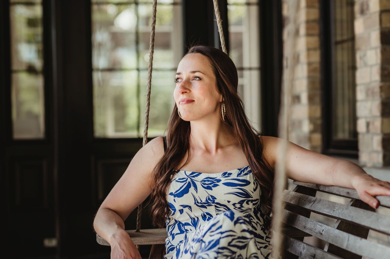 Person in floral dress sitting on porch swing in natural light.