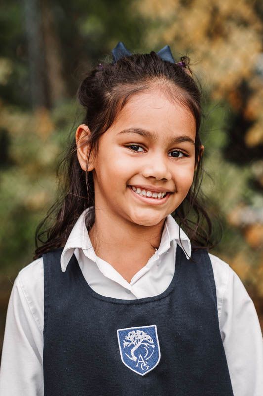 School portrait series showing child in navy uniform vest and white collar shirt with blurred autumn background.