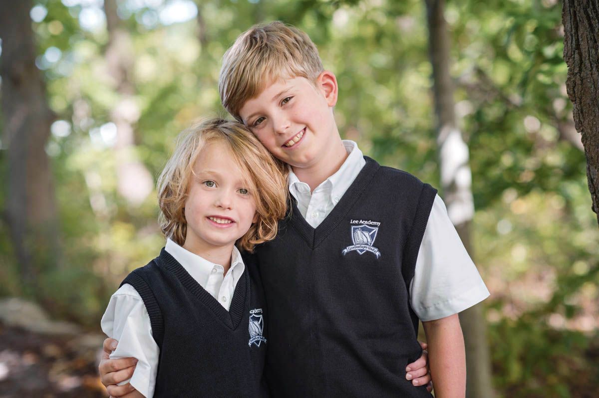 Two students in matching uniforms share candid moments outdoors in a sunlit garden setting.