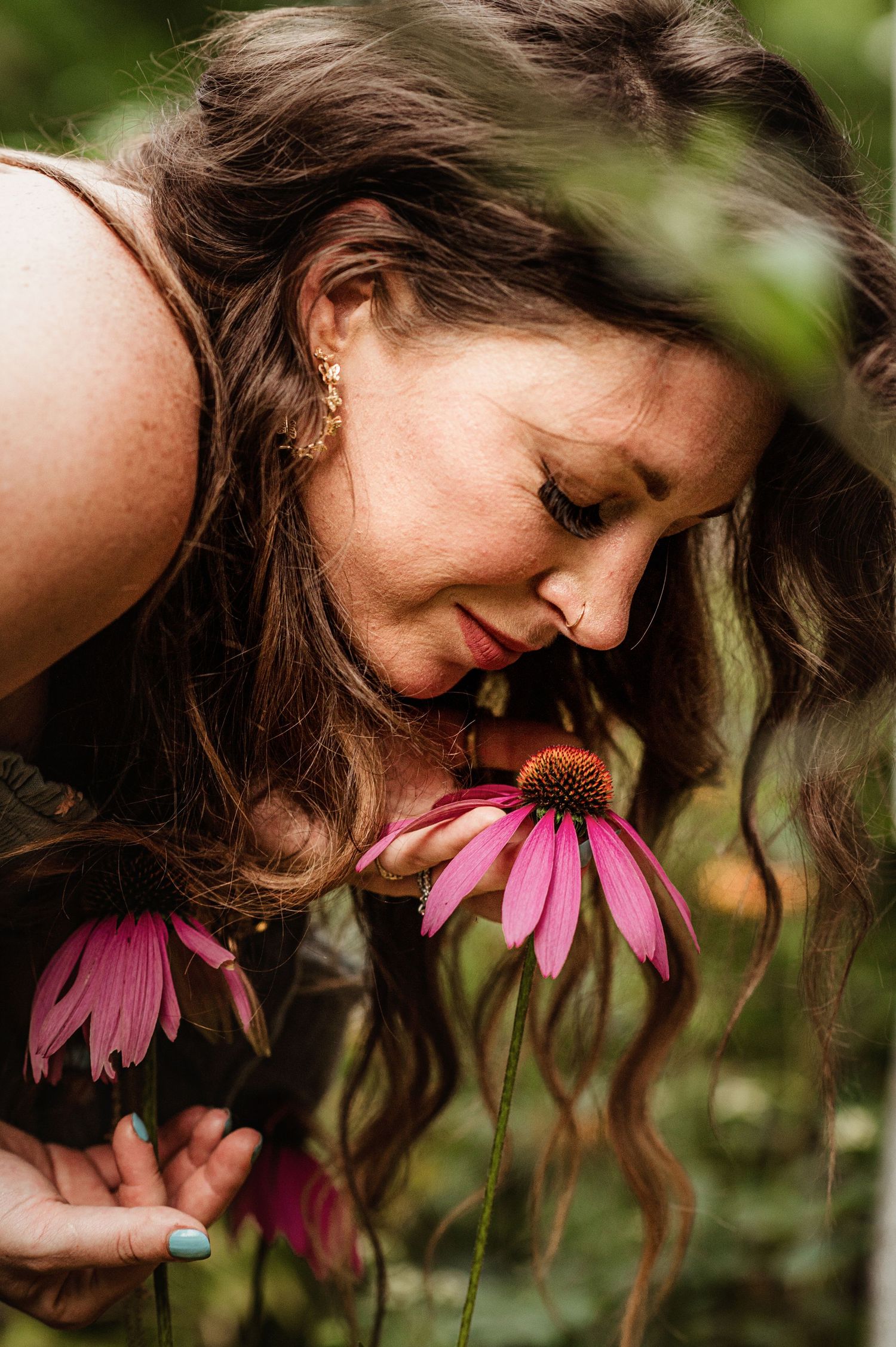 Person with long dark hair bends down to smell vibrant pink coneflowers in garden.