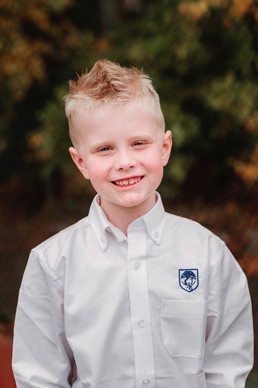 Student wearing white collared uniform shirt with school crest outdoors.