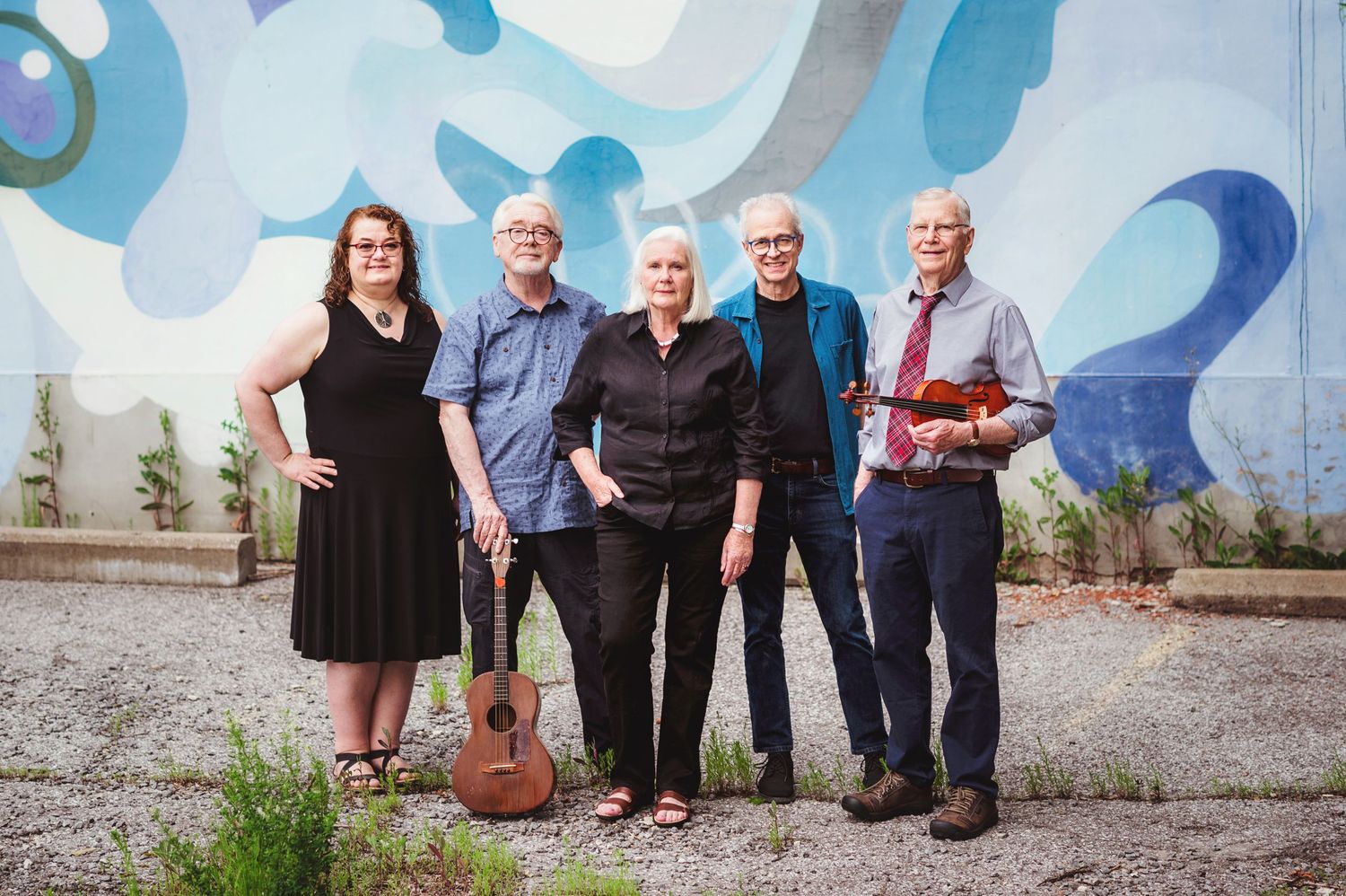 Group standing together against blue mural wall with guitar.