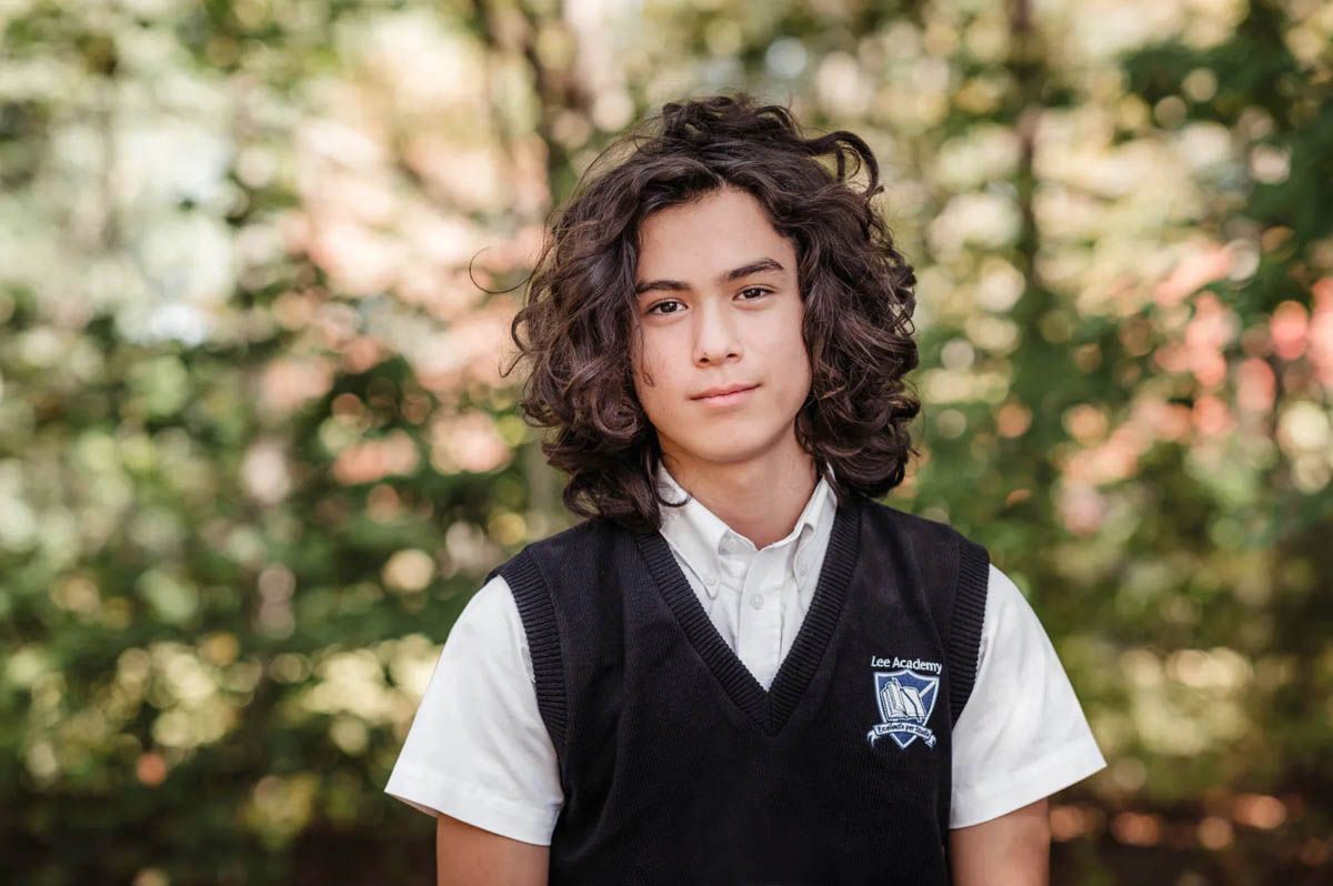 Students in white shirts and dark vests pose for school photos with trees in background.