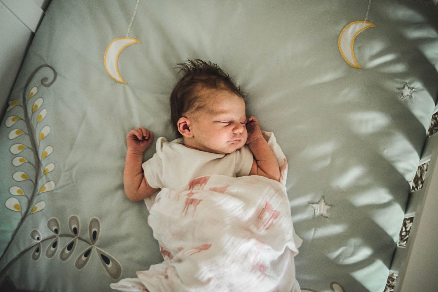 A sleeping infant rests peacefully in white bedding and natural light.