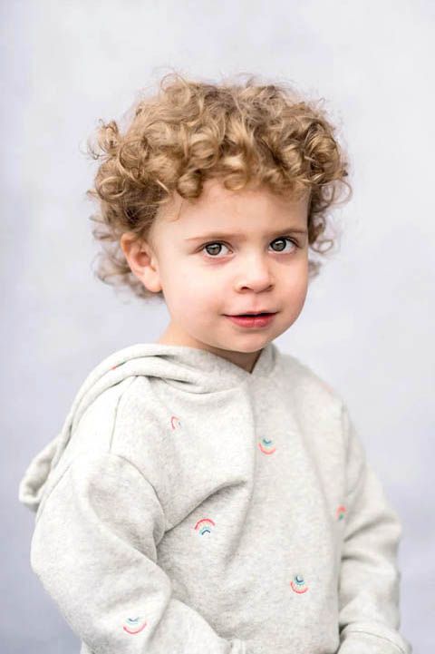 Child in light gray hoodie poses against white studio backdrop.