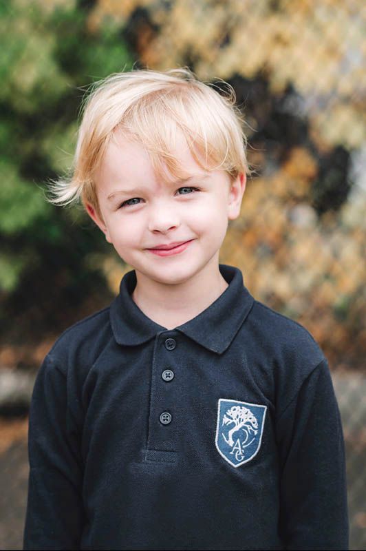 Student wearing black polo shirt with school crest smiles in outdoor portrait setting.