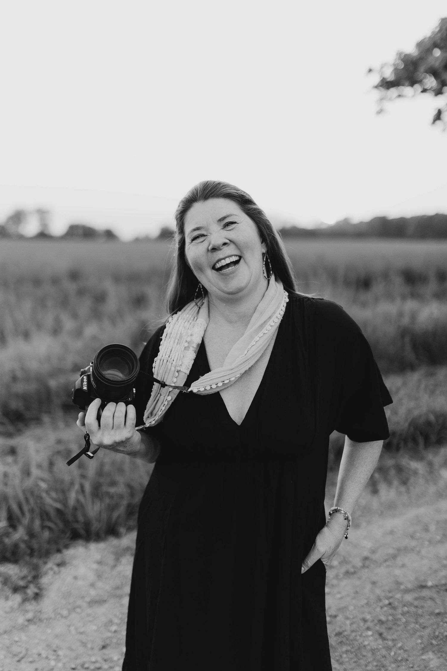 Person holding camera outdoors while laughing in black dress.
