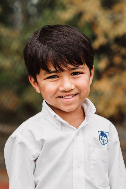 Schoolchild wearing a crisp white uniform shirt with an embroidered badge against a blurred outdoor background.