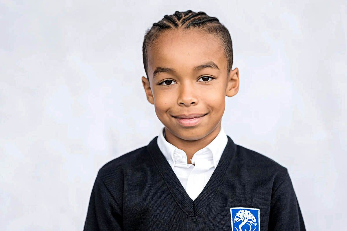 A student wearing a white collared shirt and dark blazer with school emblem poses for a portrait photo.