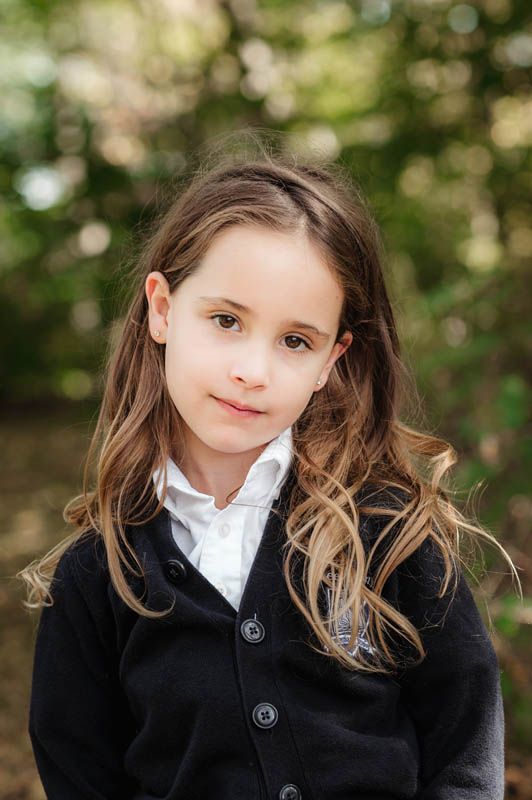 Student in a black jacket and white collar photographed outdoors with natural bokeh background.