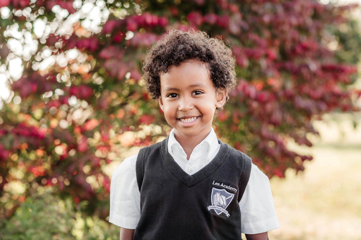 Students in matching school uniforms photographed against colorful autumn trees.