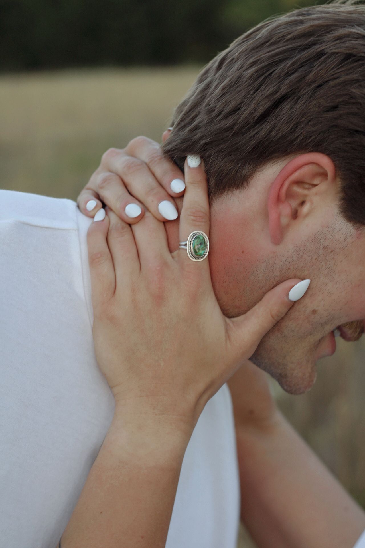 Close-up of hands with white nail polish and a statement ring in an intimate gesture.
