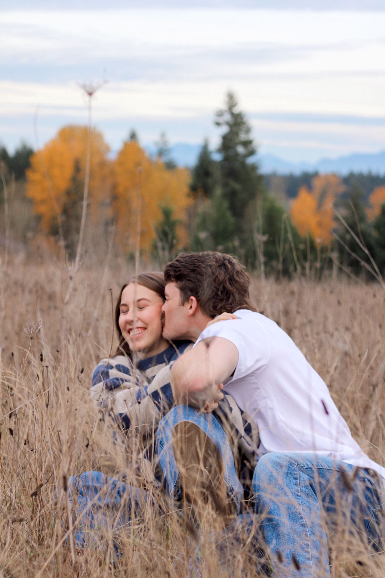A couple shares a tender moment together while sitting in a golden autumn field of tall grass at sunset.