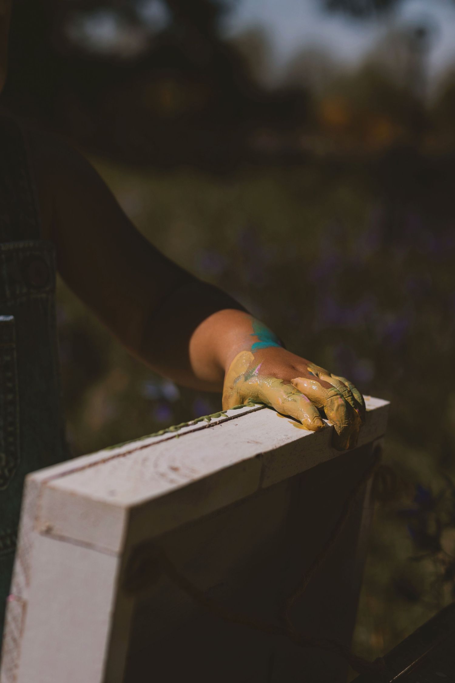 Beekeeper's gloved hand resting on a white wooden beehive box in a sunlit field of purple flowers.