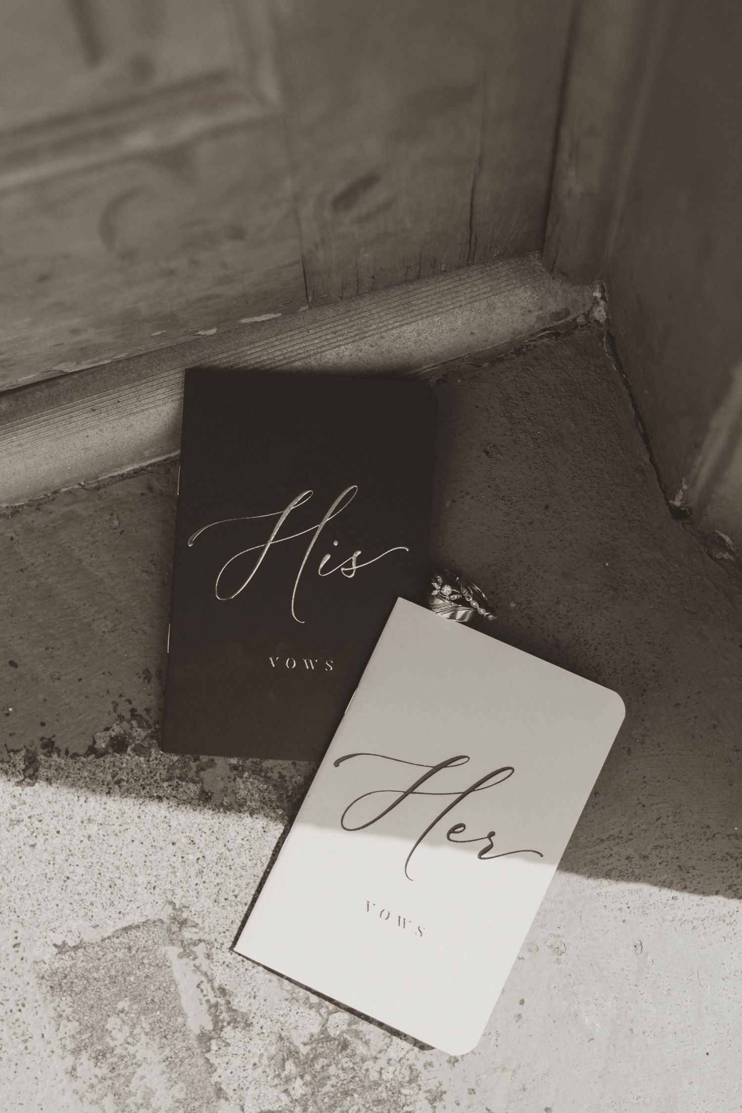 His and Her wedding vows booklets resting on stone steps in elegant black and white.