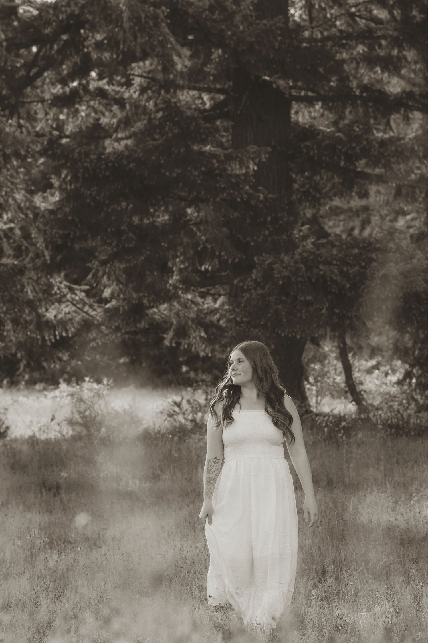 Young woman in white dress standing in a misty forest meadow, black and white photography.