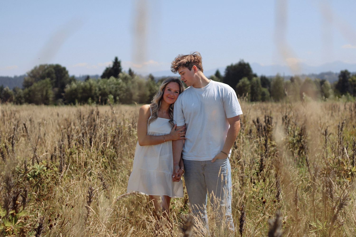 A couple walks through a golden field of tall grass on a sunny afternoon.