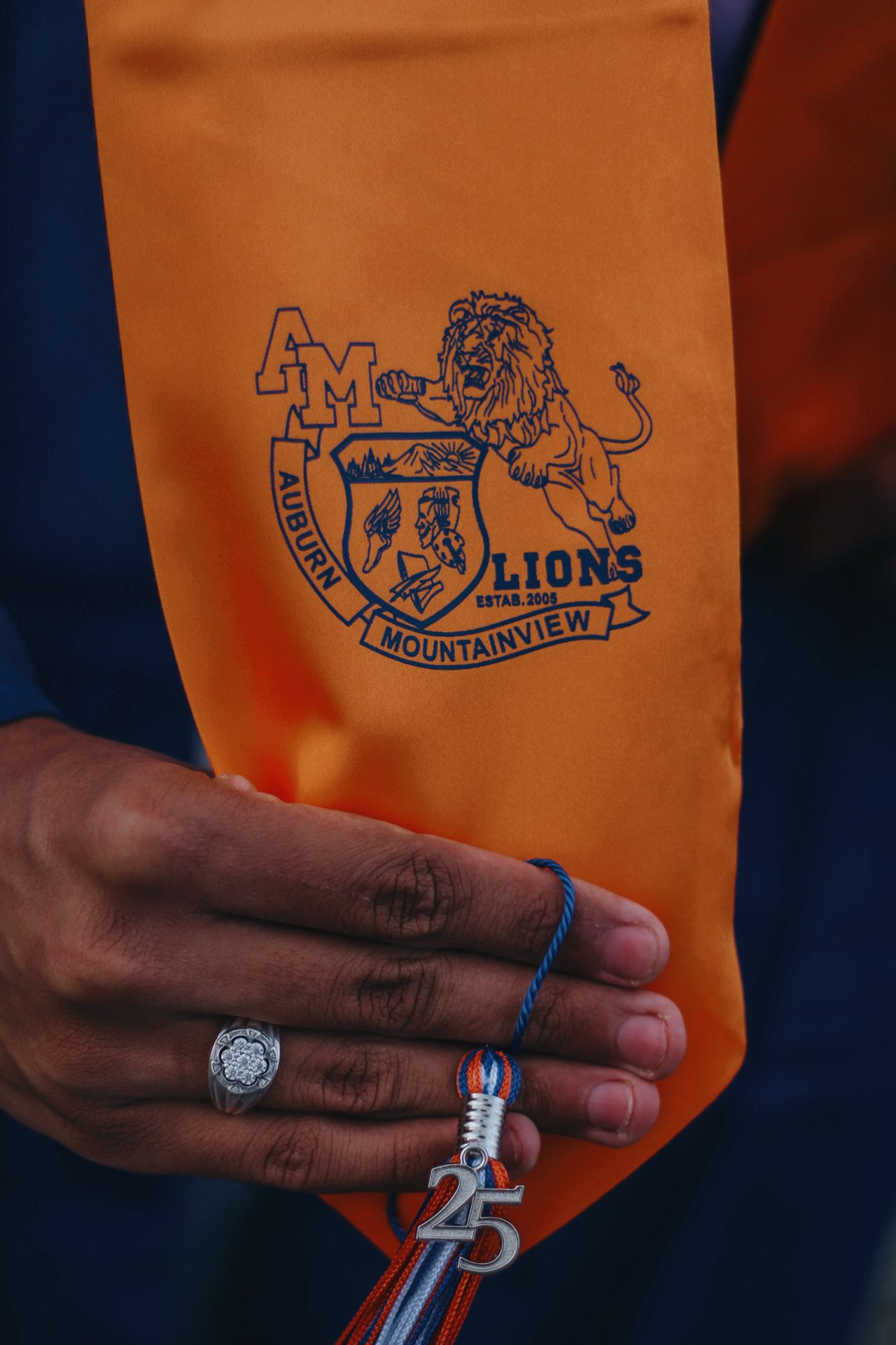 Orange graduation gown with Mountainview Lions logo and class ring detail.