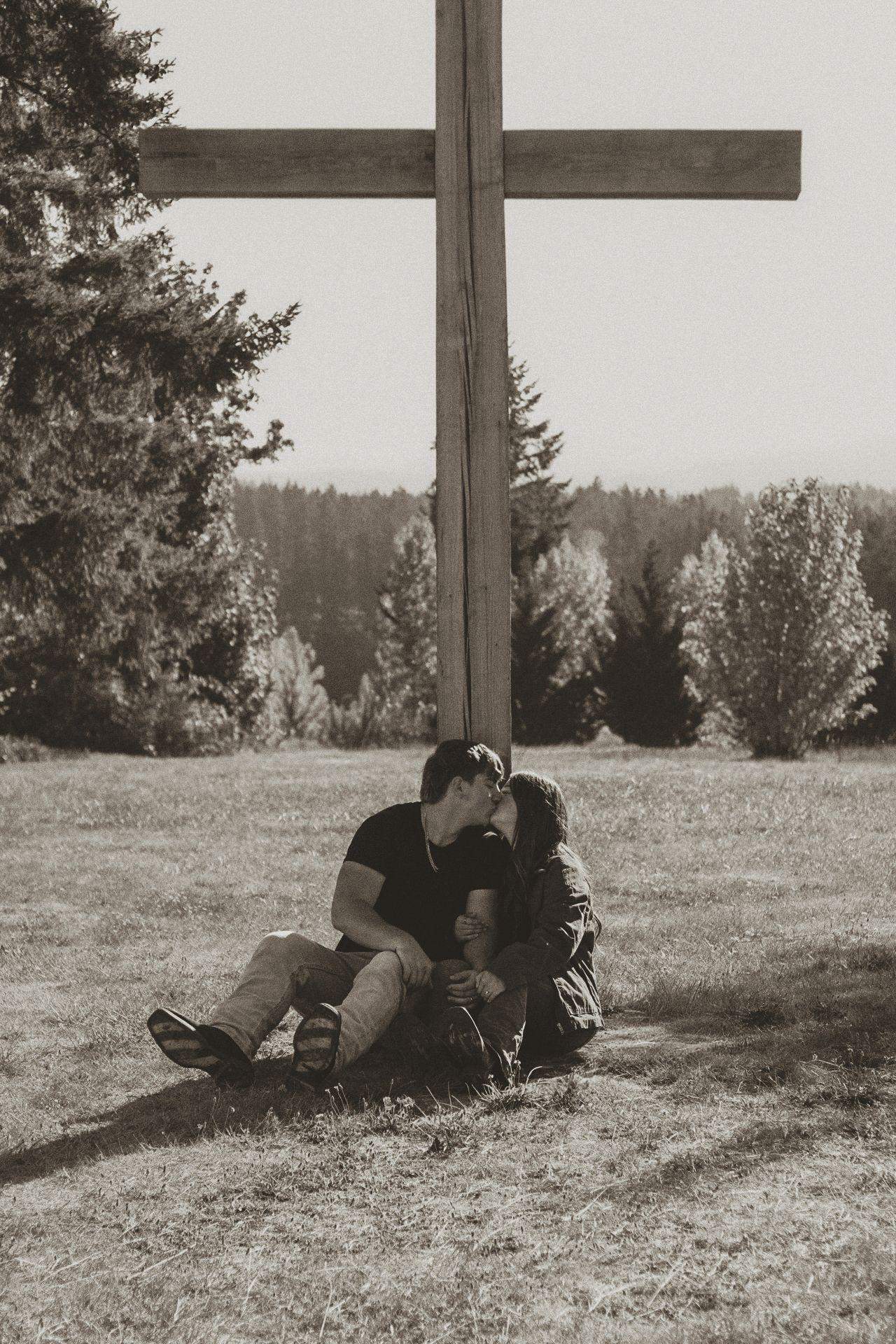 People resting by a large wooden cross on a grassy hillside.