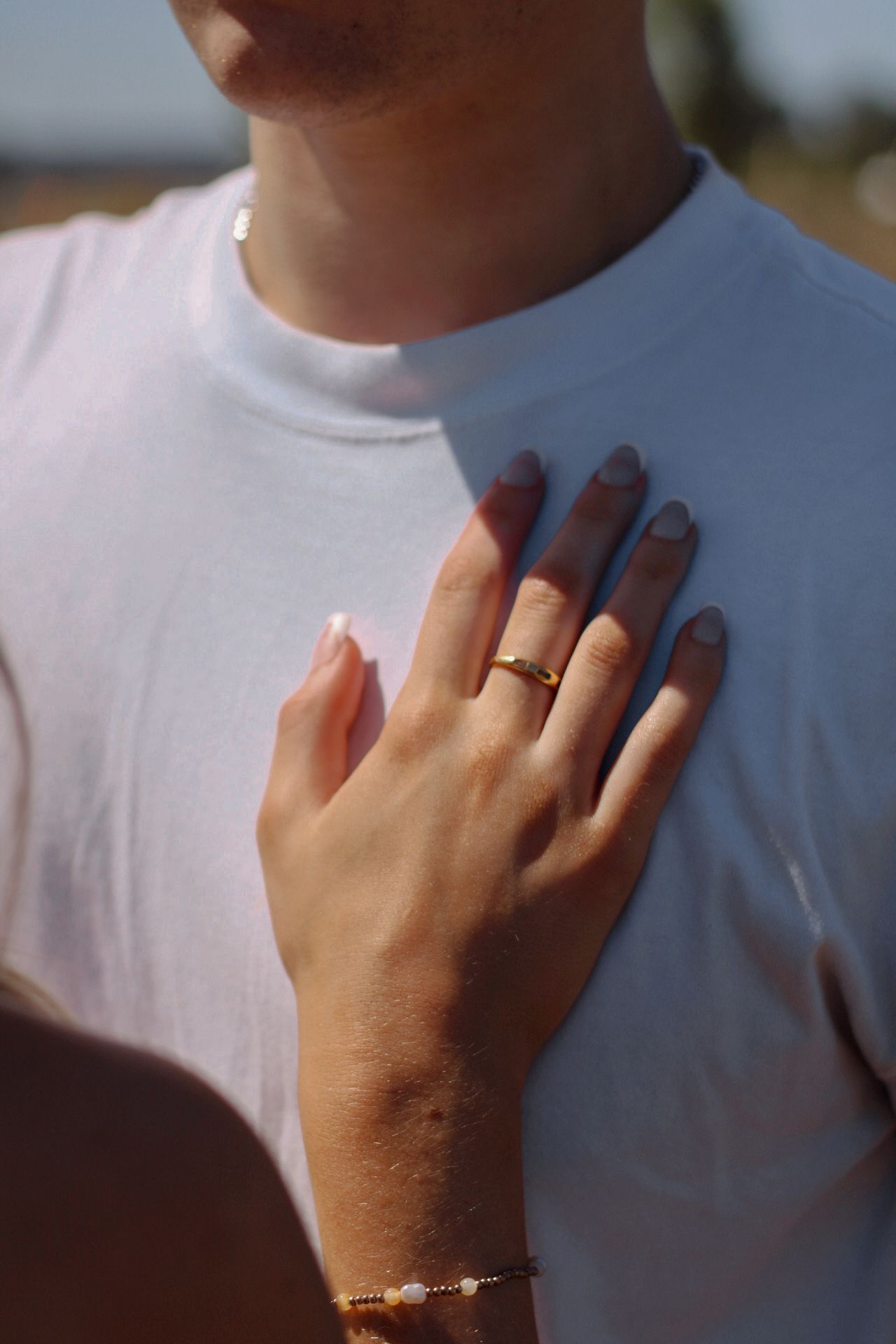 Hand with delicate jewelry and white nails resting on a white t-shirt.