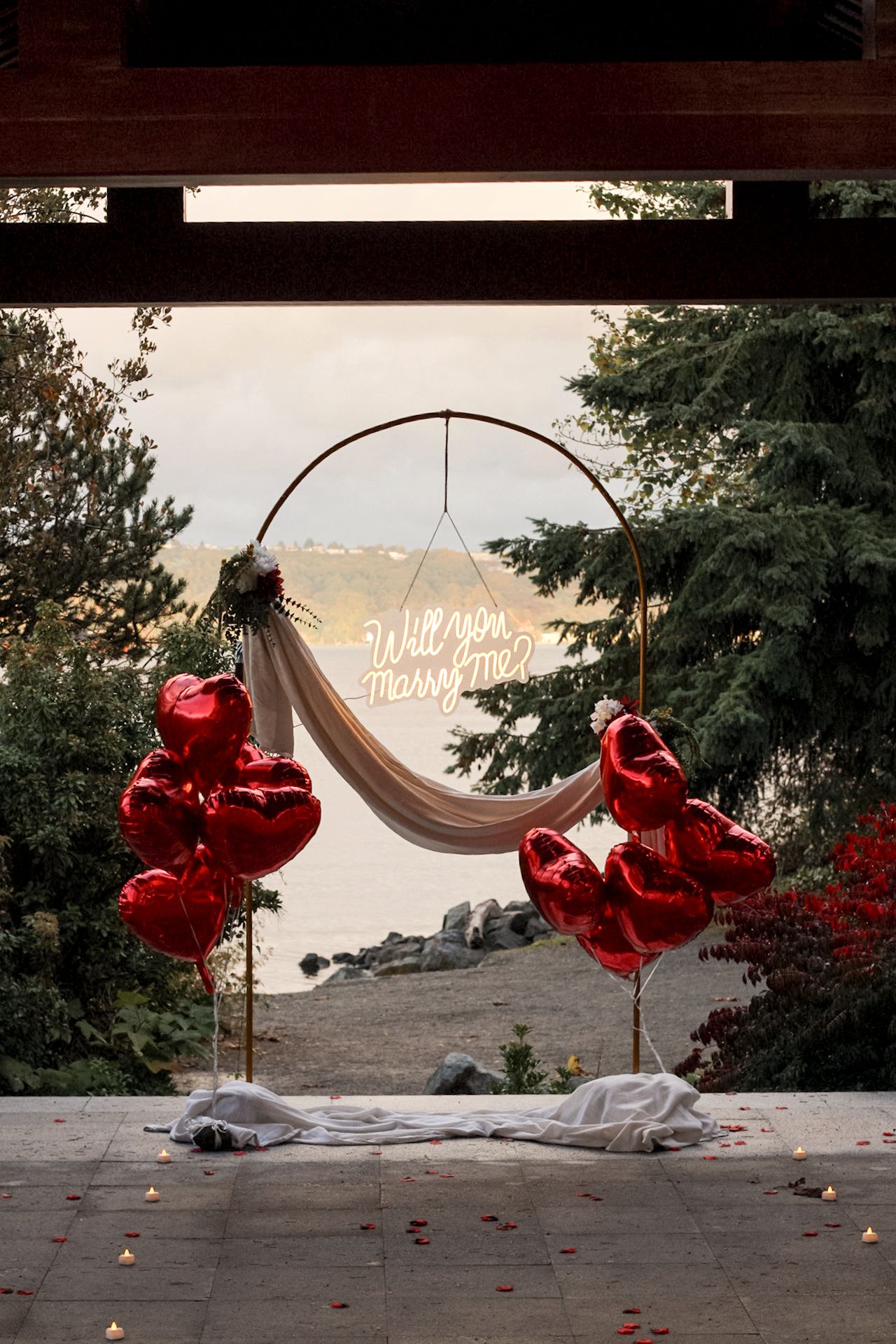 A sequence of red heart-shaped balloons floating above a white hammock against a scenic sunset backdrop.