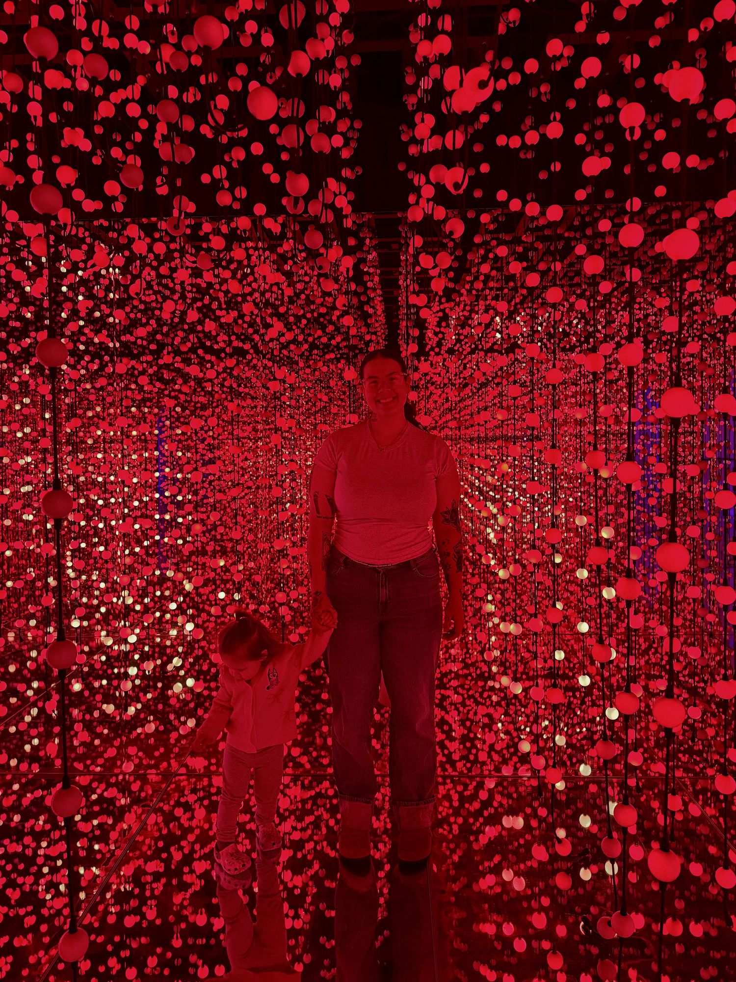 Silhouettes stand in a mesmerizing red light installation with glowing orbs creating an immersive tunnel effect.
