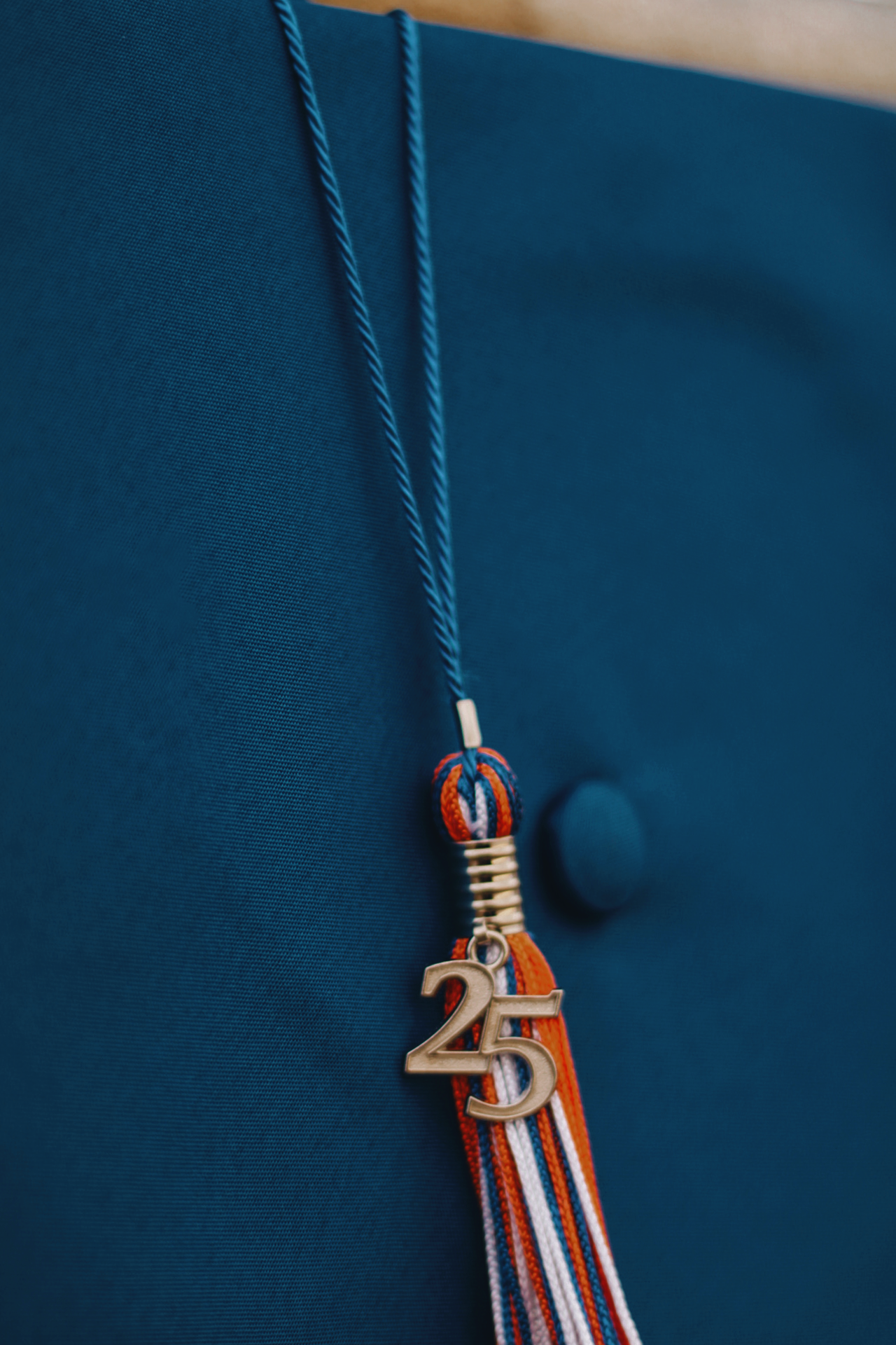 Blue graduation tassel with orange and white decorative elements hanging against dark background.