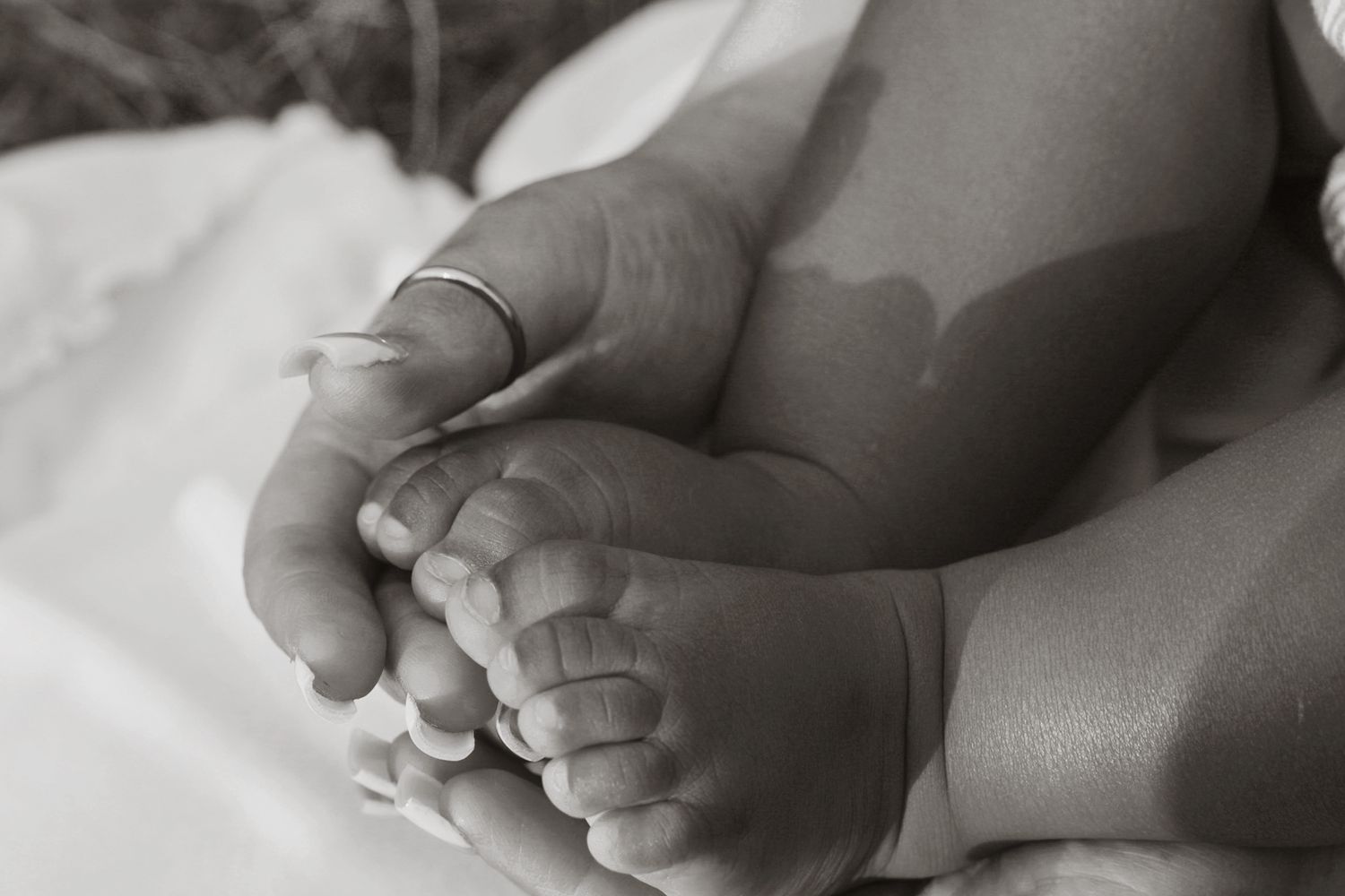 Grayscale close-up photo of tiny baby feet touching together on soft fabric.