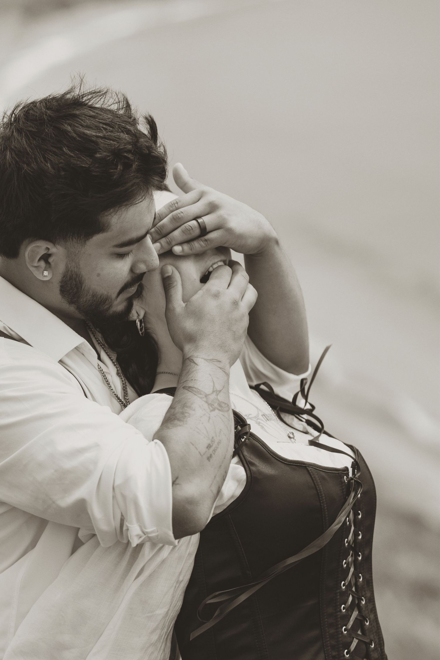 Black and white photo of a bearded man kissing a woman's hand tenderly outdoors.