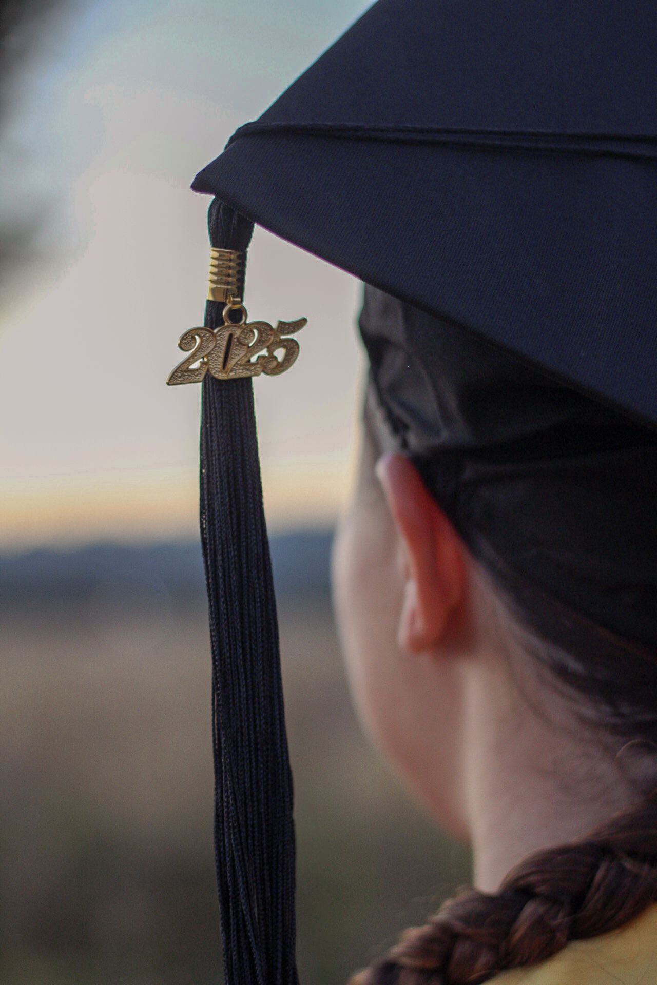 A close-up view of a graduation cap with 2025 tassel against a blurred outdoor background at sunset.