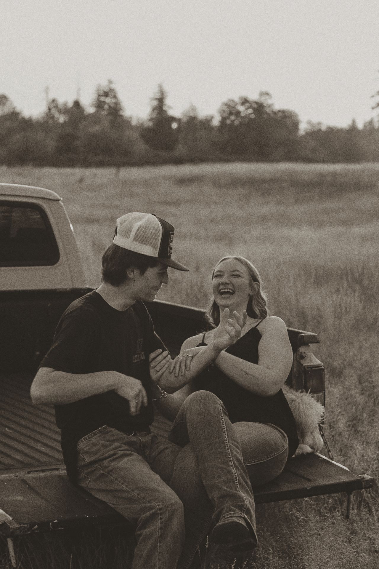 Black and white photo of a couple sharing laughter while sitting in a pickup truck bed.