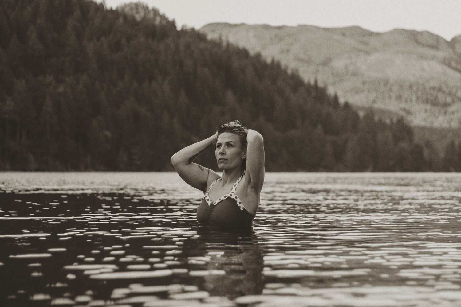 People swimming and playing in a serene mountain lake surrounded by forest.