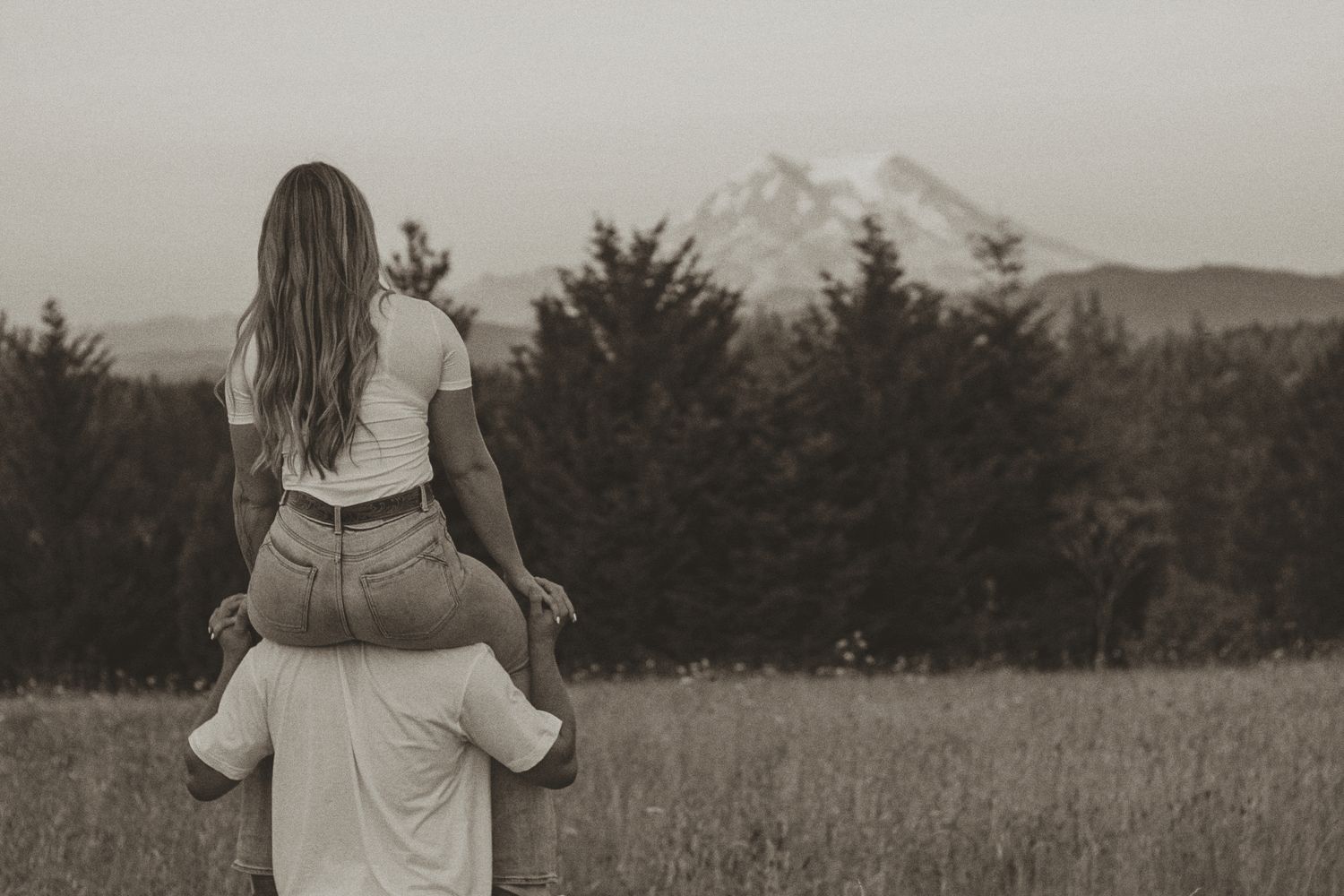 A couple walking through a meadow with mountain views in the distance.