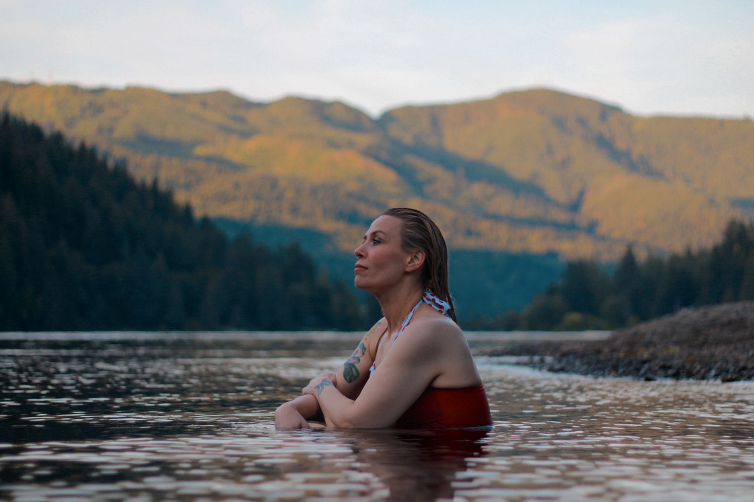 A person swimming in a scenic mountain lake during sunset.
