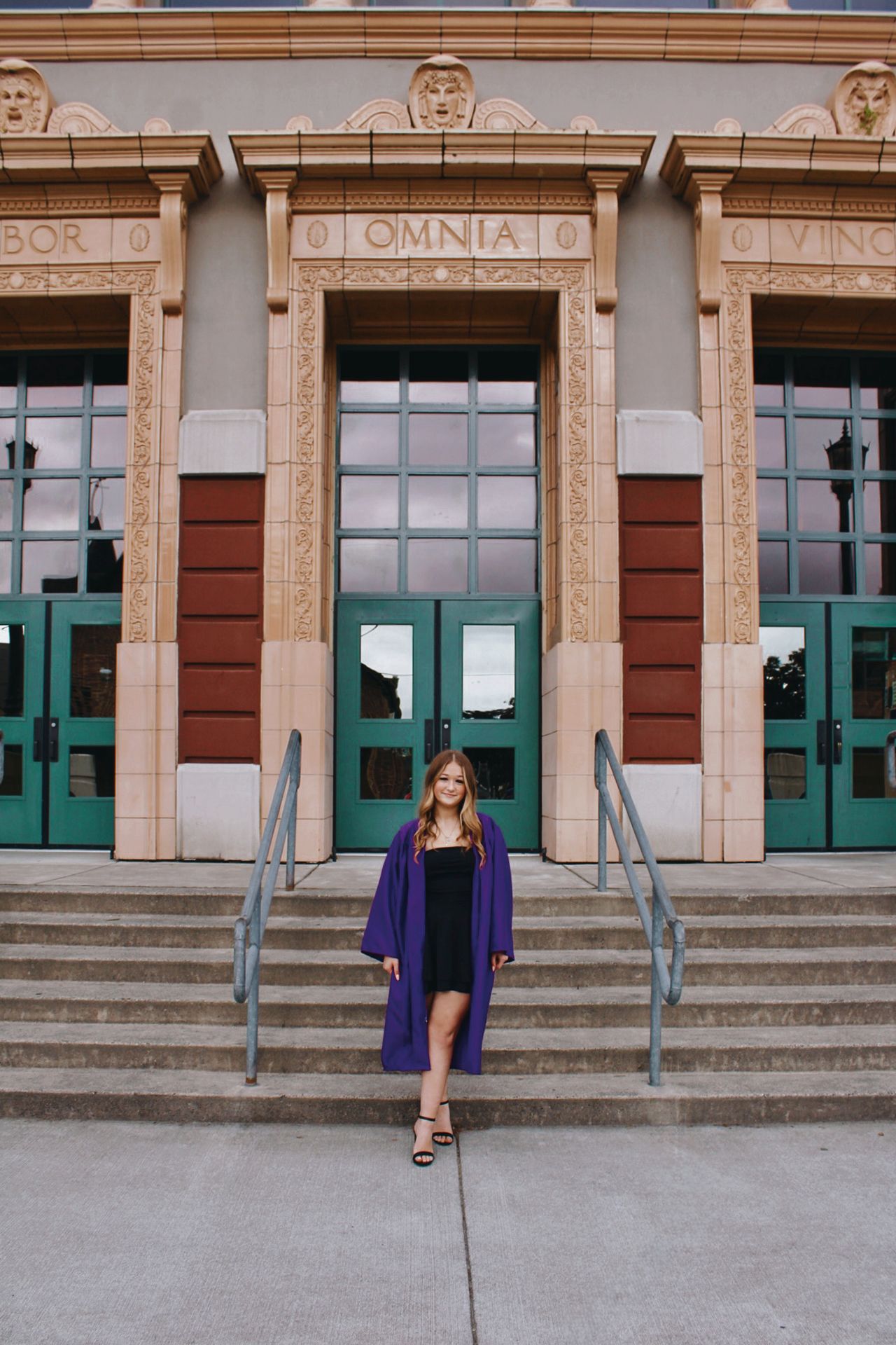 Person in purple dress standing on steps of historic building with ornate architecture.