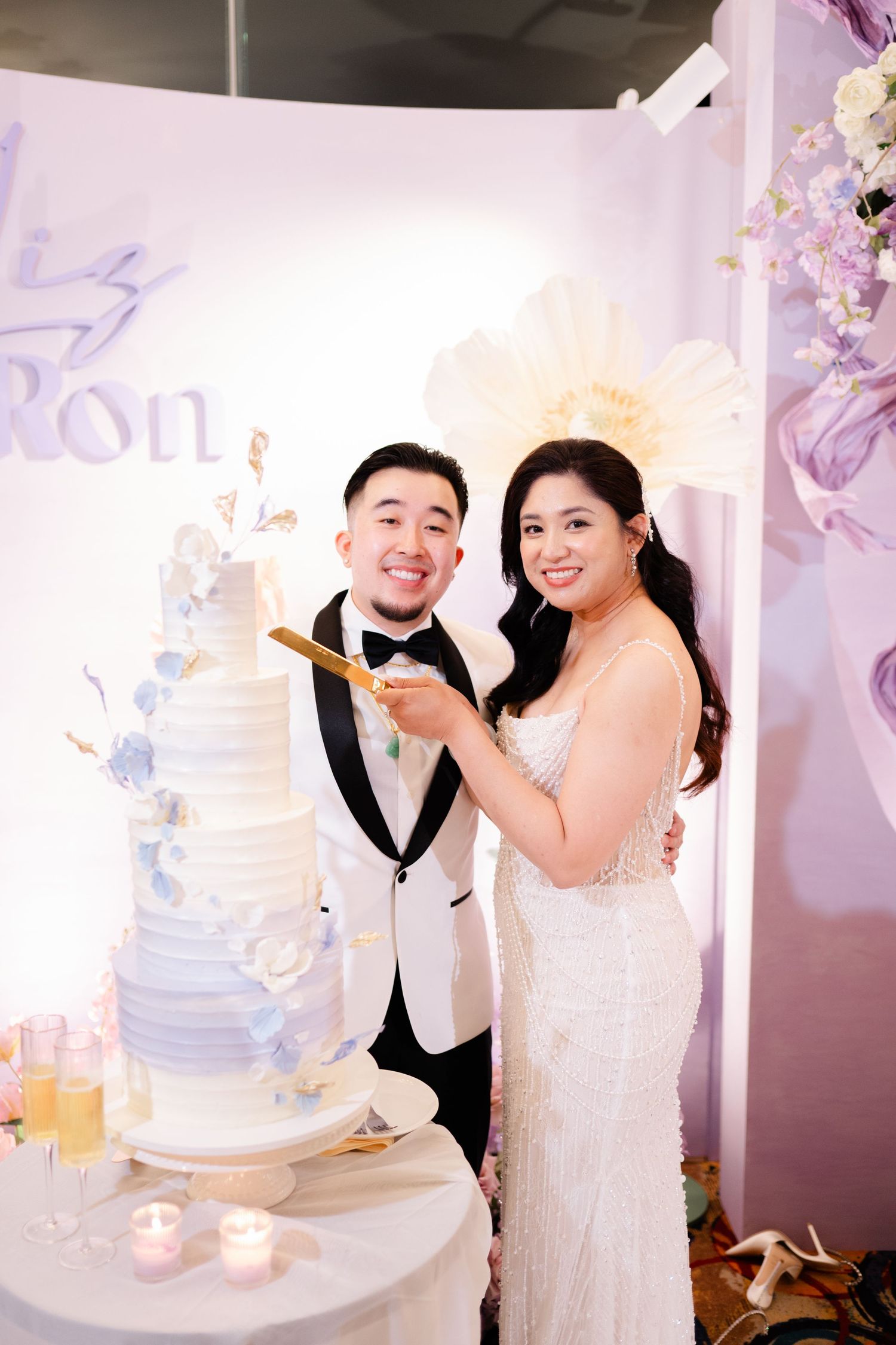Smiling bride and groom cutting elegant five-tier white wedding cake with blue floral details.