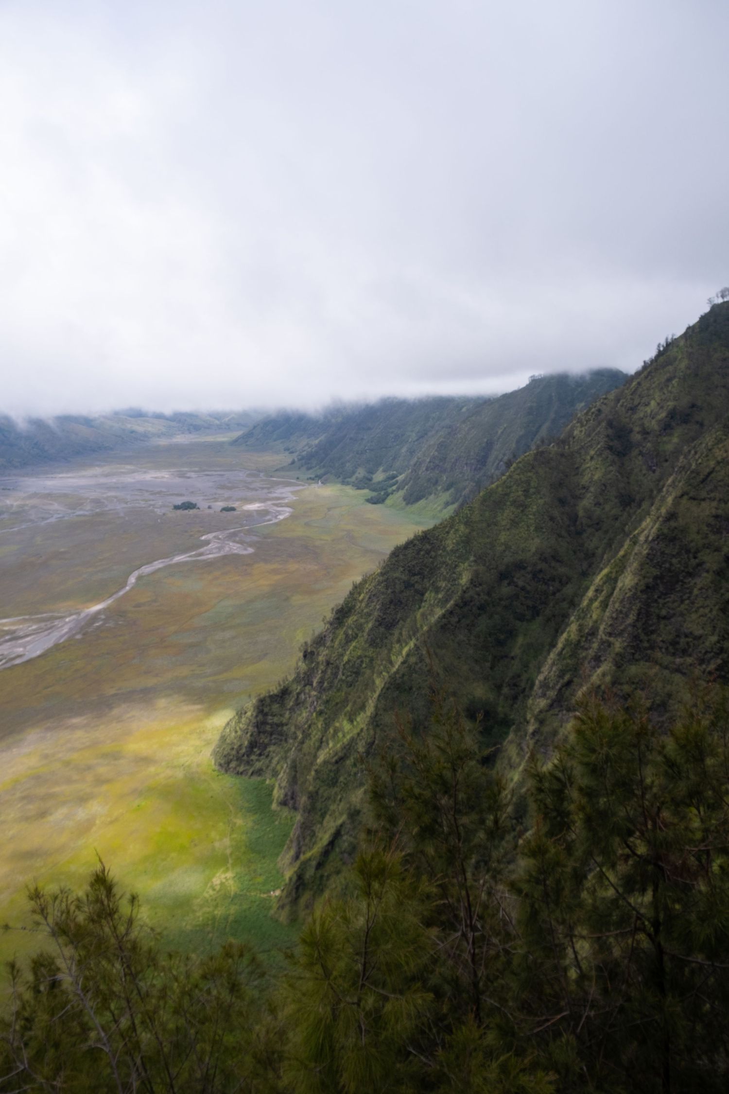 Panoramic view of a misty mountain valley with winding rivers and green slopes in a dramatic landscape.