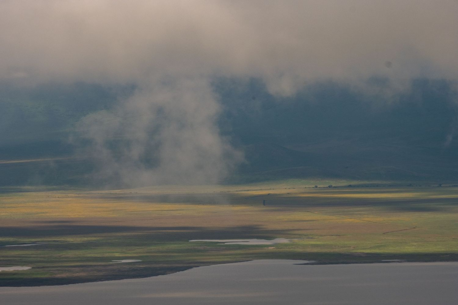 Dramatic clouds hover over sunlit plains and a winding river in an African landscape.