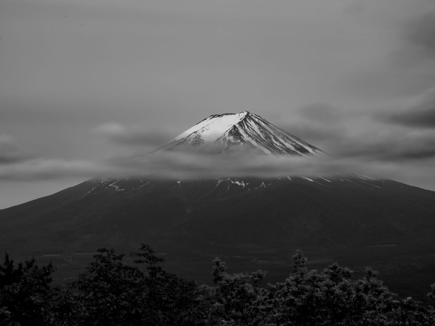 Black and white panorama of snow-capped mountain peaks against a moody sky.