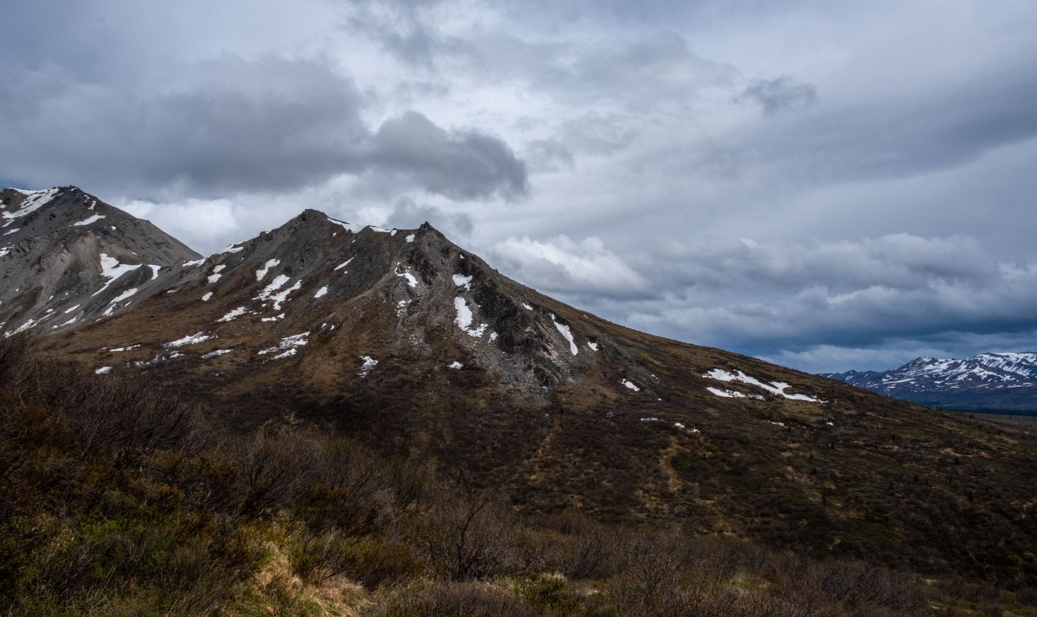Rugged mountain peaks with patches of snow under dramatic cloudy skies.
