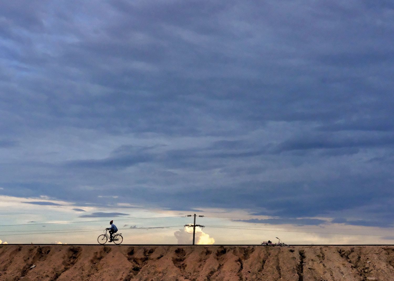 Dramatic cloudy sky with a lone cyclist silhouetted against the horizon.