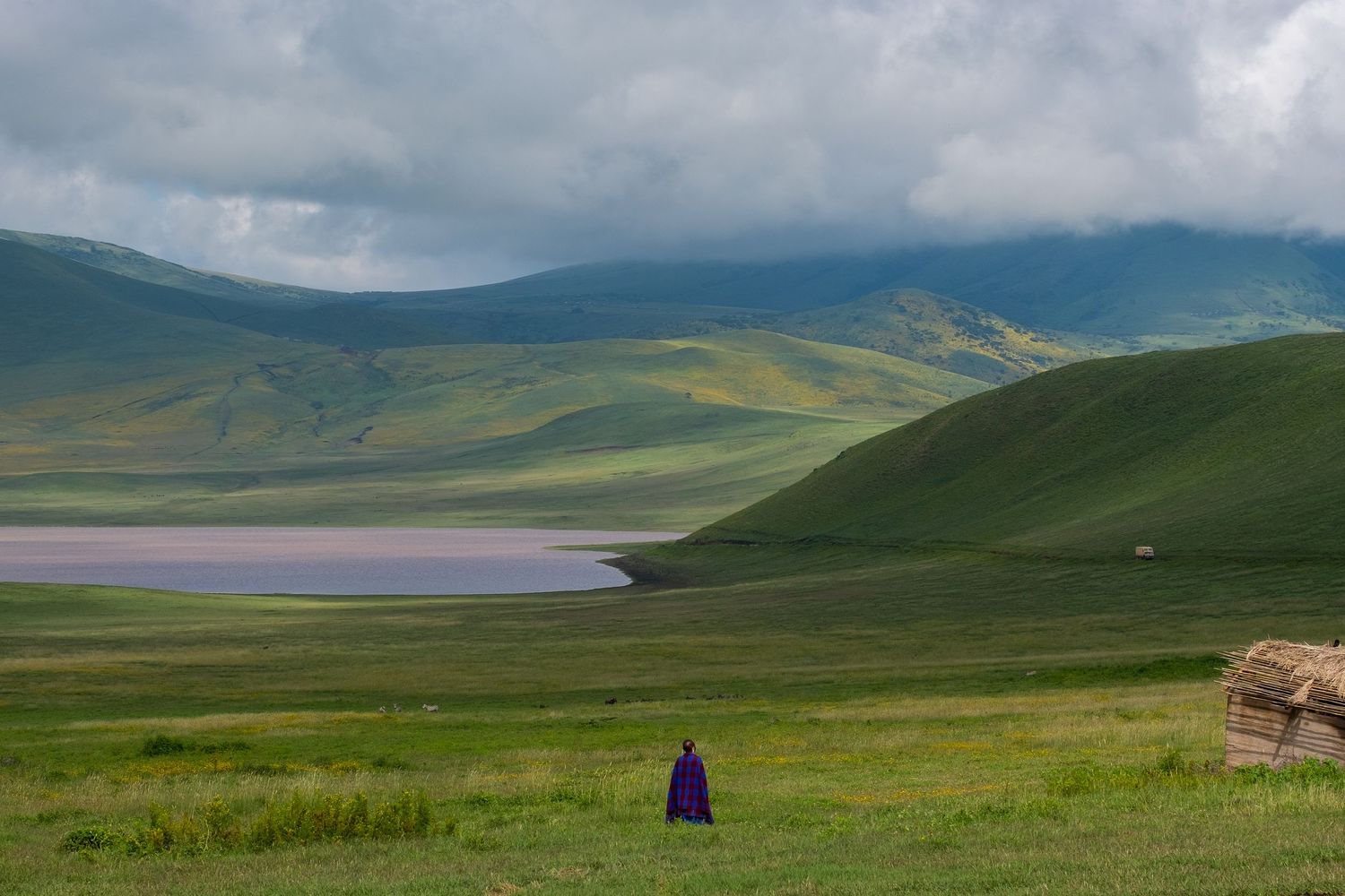 Rolling green hills and mountains stretch across a vast landscape under dramatic cloudy skies in Kyrgyzstan.